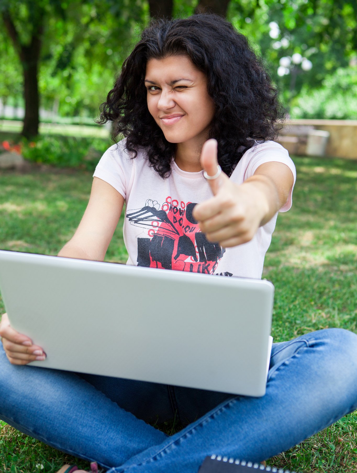 A college girl on her laptop in the park giving the thumbs up sign