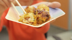[photo: hands holding a plate of takoyai dumplings]